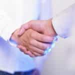 Two people in white button down collar shirts shaking hands with one another.