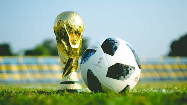 Trofi Piala Dunia di sebelah bola sepak di lapangan sepak bola.