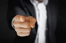 A person in a suit pointing a finger directly at the viewer.