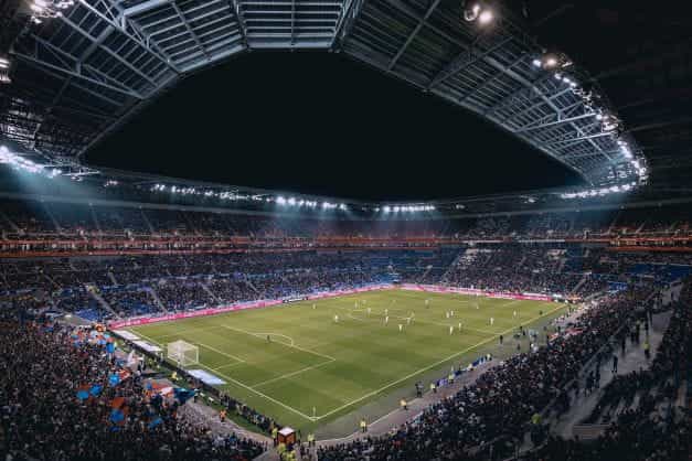 Stadion Olimpiade Lyon dari tribun penonton di tengah pertandingan yang diterangi lampu sorot.