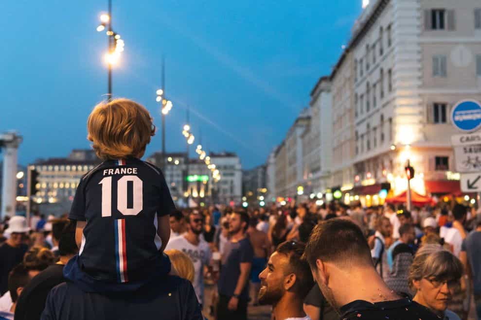 Seorang anak dengan kaus sepak bola Prancis duduk di bahu seorang pria di luar stadion.