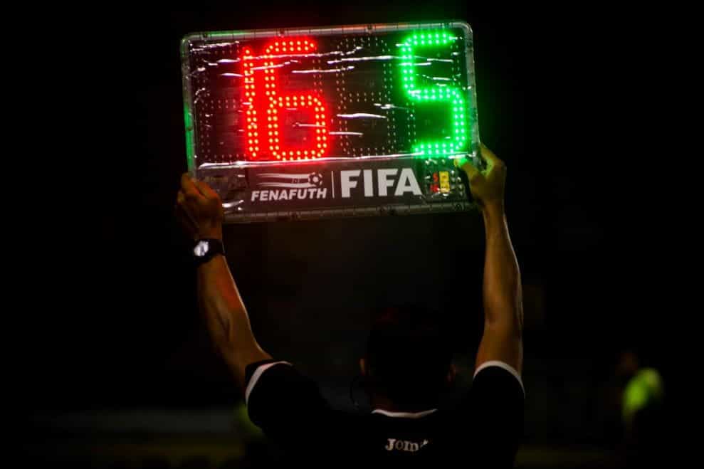 Wasit keempat mengangkat papan yang menunjukkan pergantian pemain selama pertandingan sepak bola di malam hari.