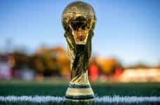 The FIFA World Cup trophy placed on the touchline of a football field.