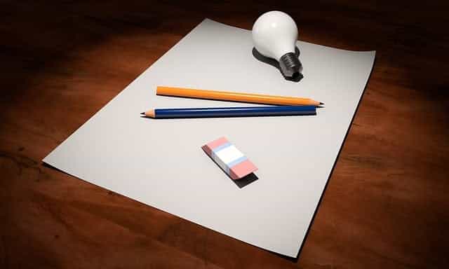 Selembar kertas putih kosong diletakkan di atas meja, dengan dua pensil, penghapus dan bola lampu diletakkan di atasnya.
