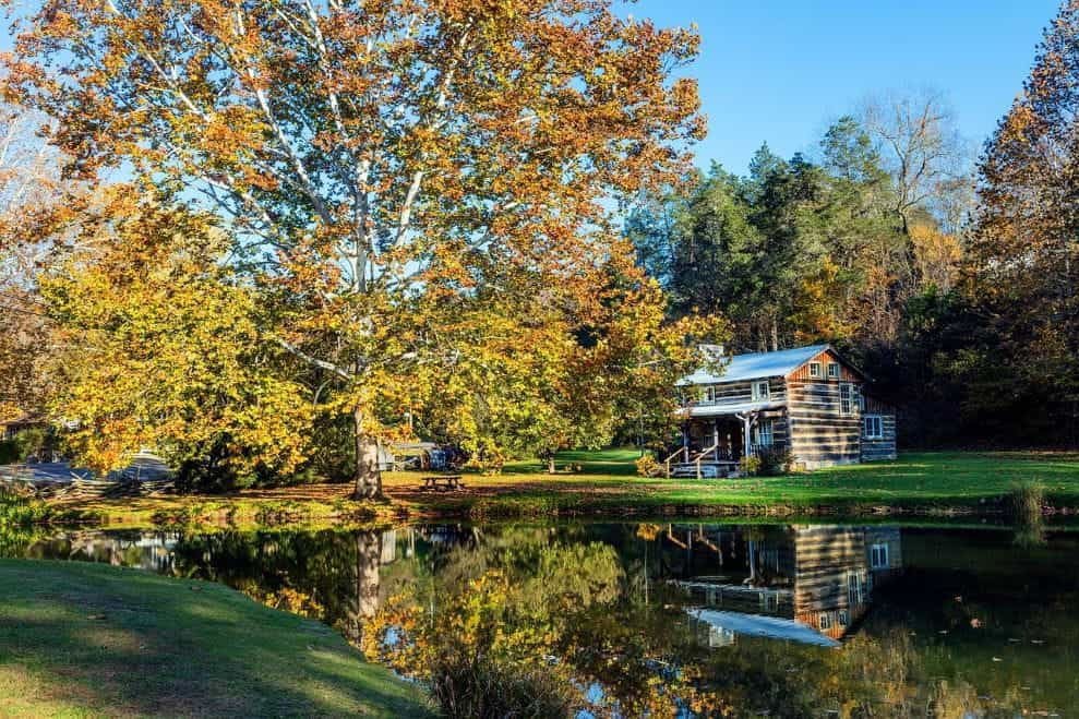 Sebuah pondok kayu kecil di sebelah pohon besar dan kolam kecil di pedesaan Virginia Barat selama musim gugur.