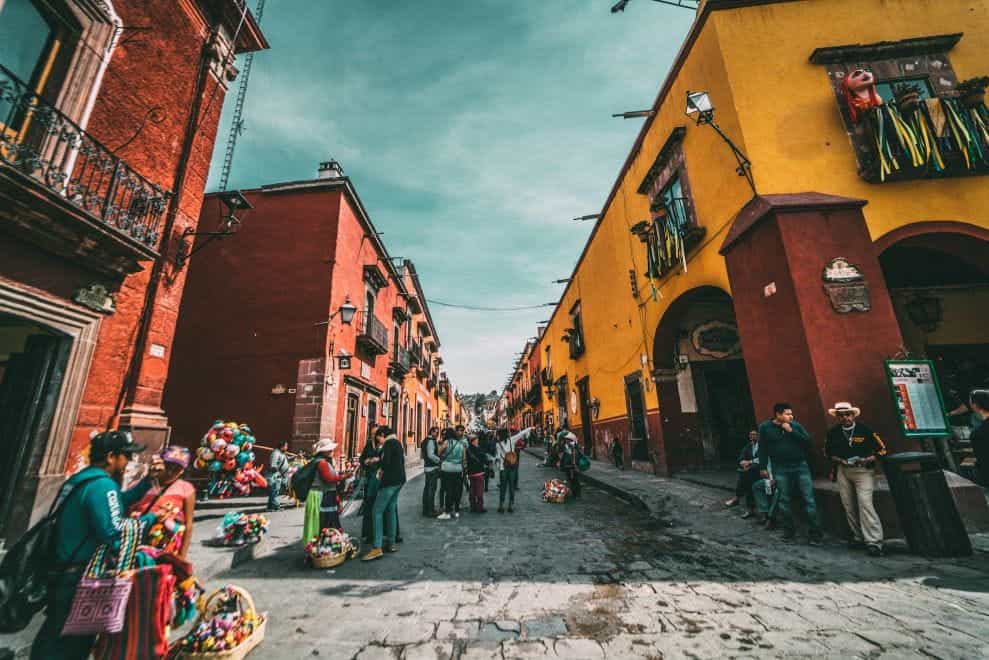 Orang-orang berdiri di jalan di antara gedung-gedung penuh warna di San Miguel de Allende, Meksiko.