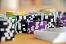 Several different stacks of black, yellow, green and purple poker chips on a table, stacked next to a deck of playing cards.