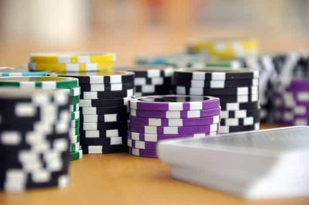 Beberapa tumpukan berbeda dari chip poker hitam, kuning, hijau dan ungu di atas meja, ditumpuk di sebelah setumpuk kartu remi.