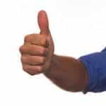 A person’s outstretched arm in a blue rolled up sleeve giving a thumbs up.