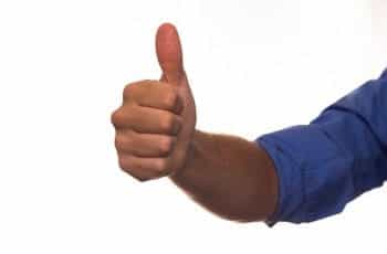 A person’s outstretched arm in a blue rolled up sleeve giving a thumbs up.