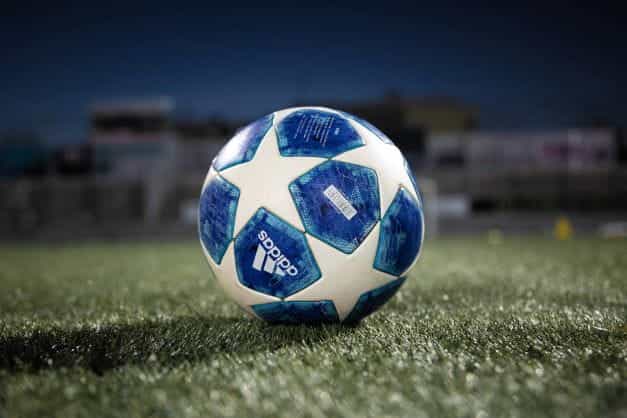 Liga UEFA biru dan putih statis bermerek sepak bola Adidas di atas rumput, di bawah lampu sorot.