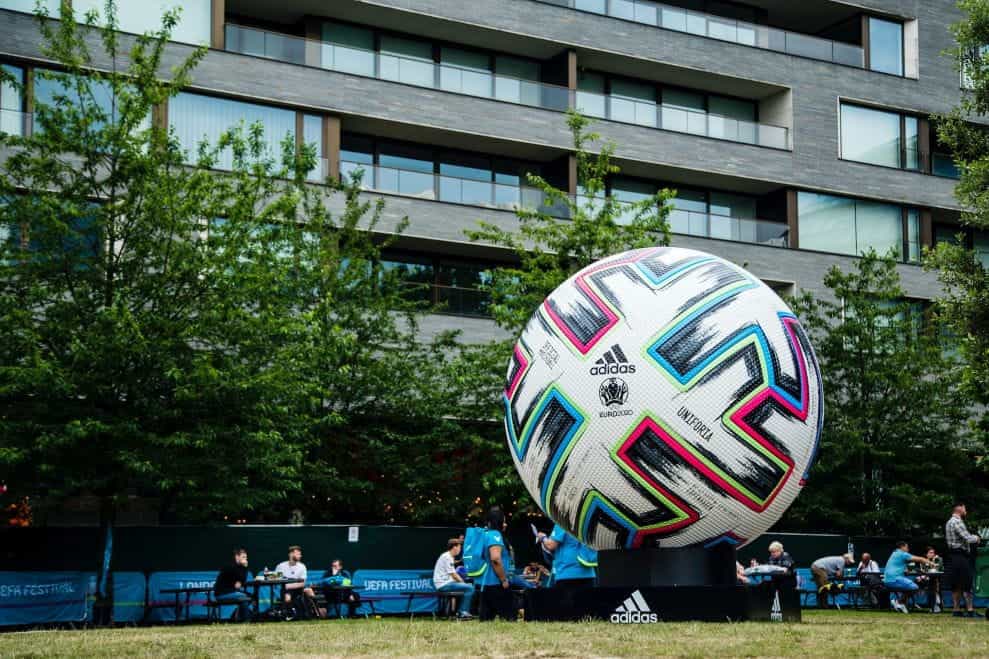 Sepak bola Adidas multiwarna dengan merek UEFA Euro 2020 di atasnya, dengan acara UEFA di latar belakang.