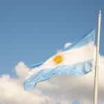 The Argentinian flag waves in front of a blue sky with white clouds.
