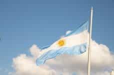 The Argentinian flag waves in front of a blue sky with white clouds.