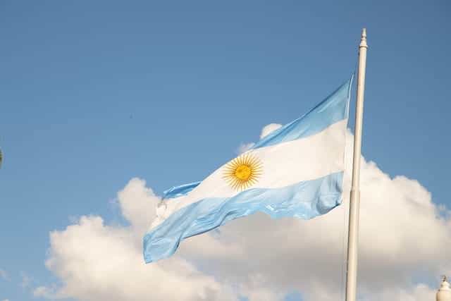 Bendera Argentina melambai di depan langit biru dengan awan putih.