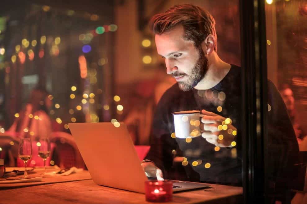 Seorang pria minum secangkir kopi dan menggunakan laptop.