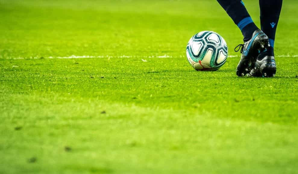 Seseorang berdiri siap untuk menendang bola sepak di lapangan hijau.