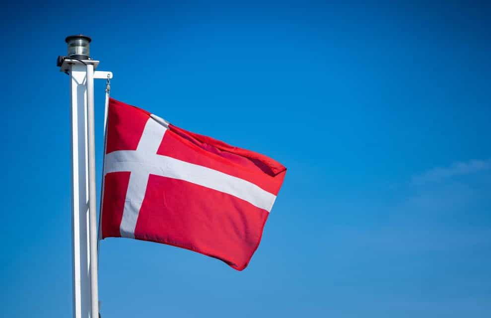 Bendera Denmark dipasang di tiang putih dengan latar belakang langit biru.