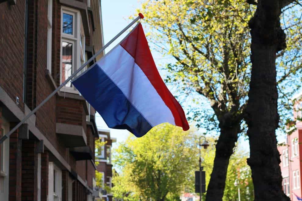 Bendera Belanda ditempelkan pada tiang miring di depan sebuah bangunan bata.
