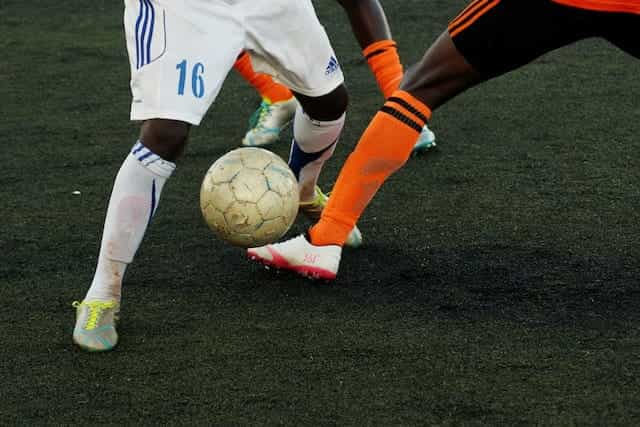 Tiga pemain sepak bola memperebutkan penguasaan bola di lapangan hijau.