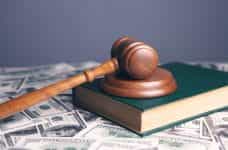 A wooden gavel sits on a book on top of a table covered in paper money.