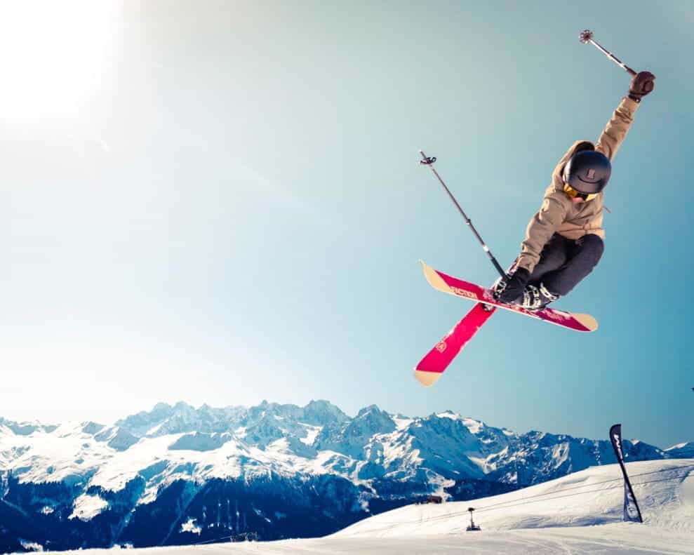 Seorang pria berjaket coklat dan peralatan ski bersiap untuk mendarat di atas salju.