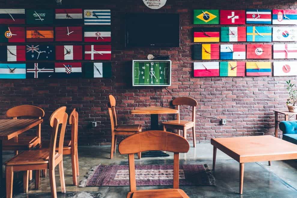 Sebuah kafe dengan bendera berbagai negara membentuk kisi-kisi di dinding di kedua sisi TV yang dimatikan dan jam bertema lapangan sepak bola.