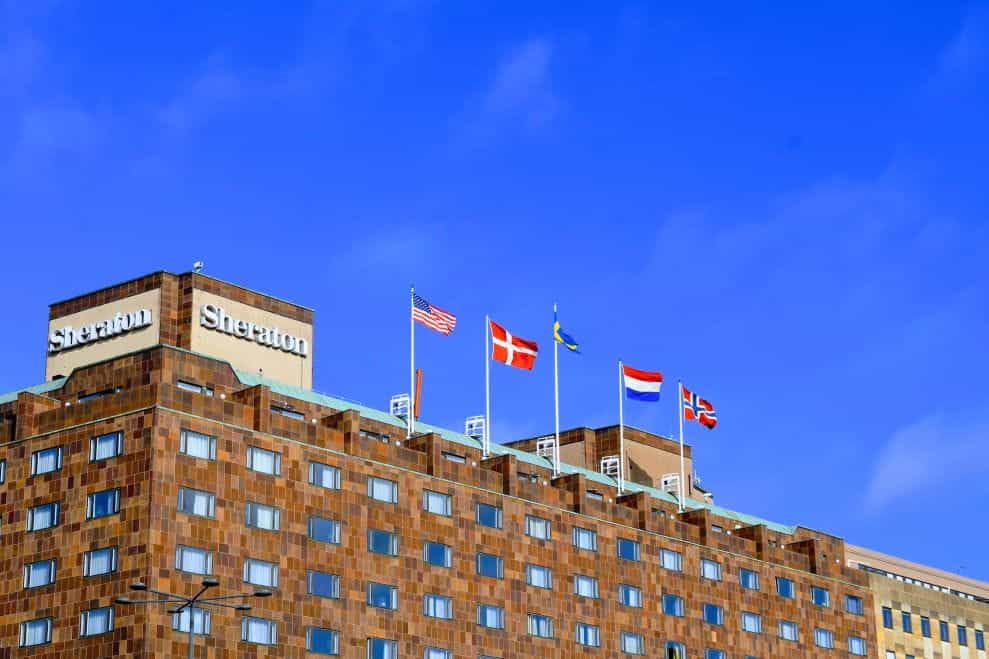 Bagian depan gedung Sheraton dengan bendera Amerika Serikat, Denmark, Swedia, Belanda dan Norwegia di atapnya.
