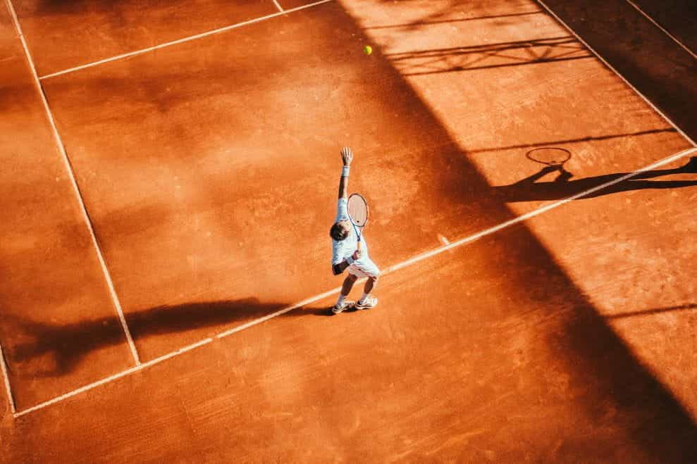 Seorang pemain tenis di lapangan keras memasuki langkah servisnya.