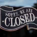 A black and white sign on a glass door reads SORRY WE ARE CLOSED.