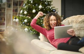 A smiling and happy lady celebrates a winner while watching an event on her tablet led on the sofa.