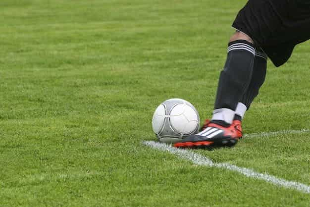 Seorang pemain sepak bola menendang bola di lapangan rumput.