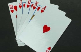 Five playing cards in the same suit of hearts lying flat on a grey surface.
