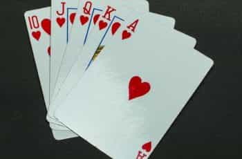 Five playing cards in the same suit of hearts lying flat on a grey surface.
