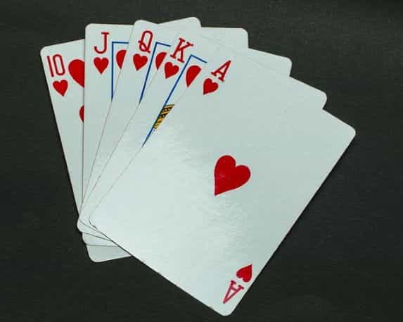 Lima kartu remi dengan jenis hati yang sama tergeletak rata di permukaan abu-abu.