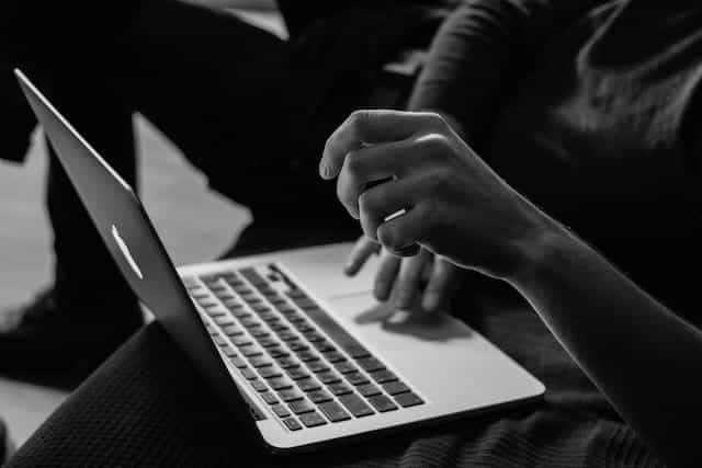 Sebuah laptop menyeimbangkan lutut seseorang saat mereka menggunakan keyboard.