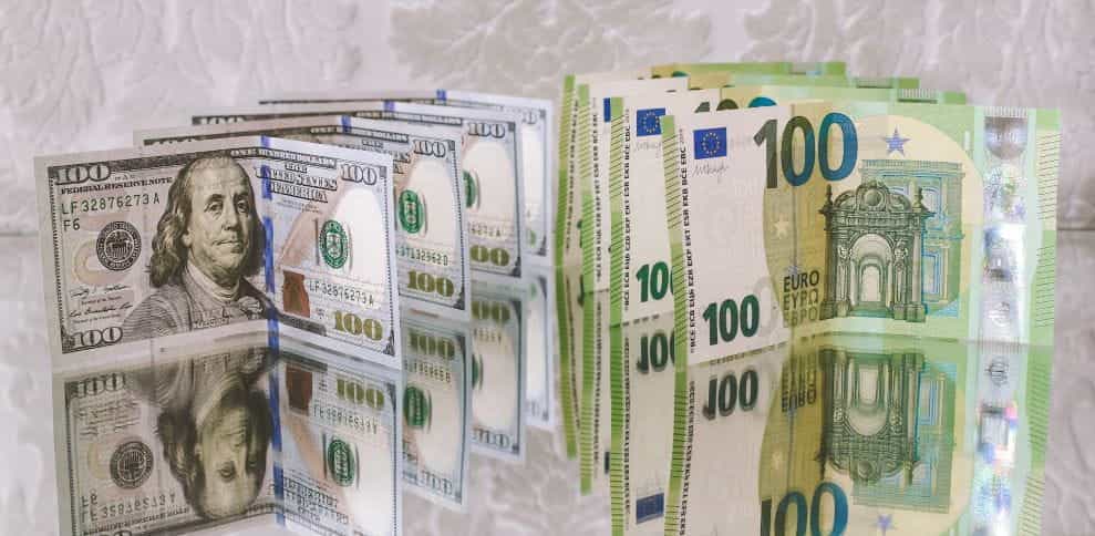 Tumpukan uang 100 dolar dan 100 euro tetap tegak di permukaan reflektif.