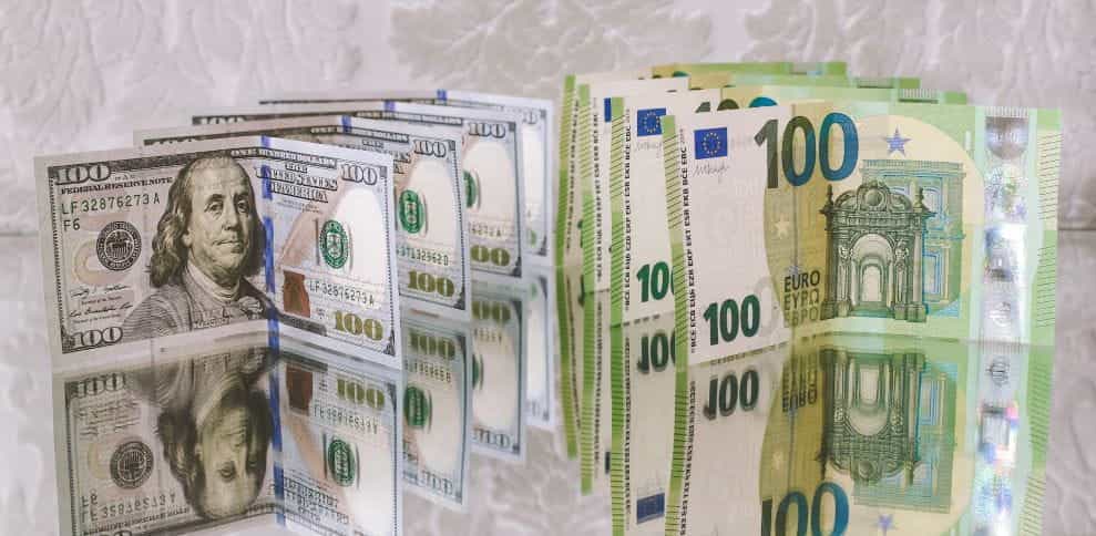 Stacks of 100-dollar and 100-euro bills kept upright on a reflective surface.