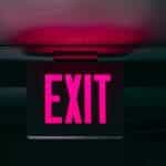 A neon pink exit sign against a dark backdrop.