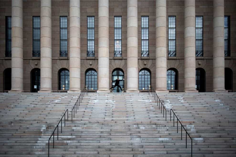 The steps leading into the Finland Parliament with one man gesturing at the top of the stairs.