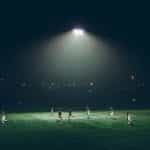 A group of football players playing under floodlights.