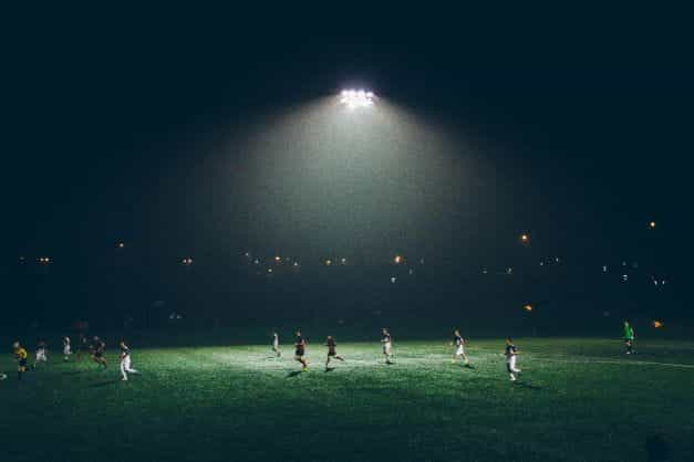 Sekelompok pemain sepak bola bermain di bawah lampu sorot.