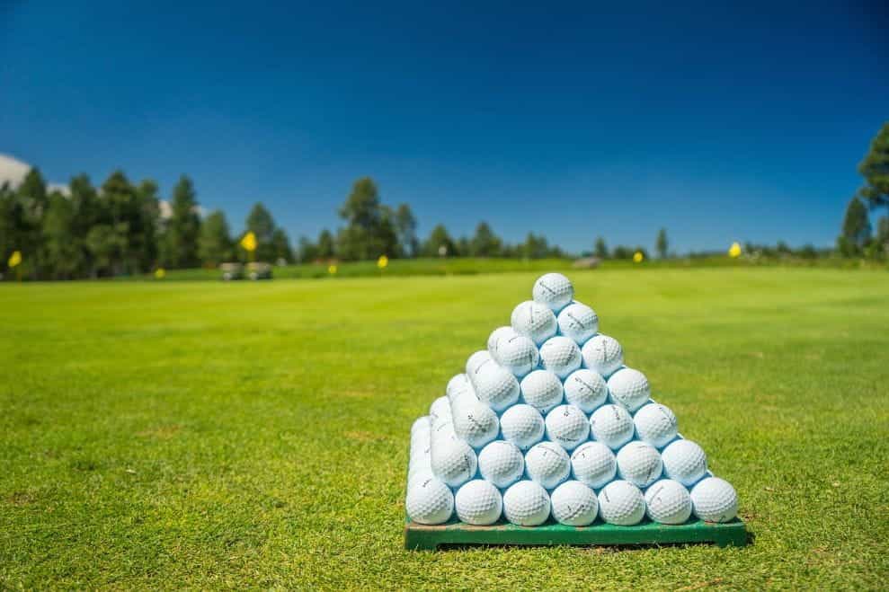 Piramida tumpukan bola golf yang diletakkan di atas lapangan golf di luar ruangan.