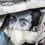 A face printed on a banknote is visible through crumpled up banknotes.