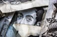 A face printed on a banknote is visible through crumpled up banknotes.