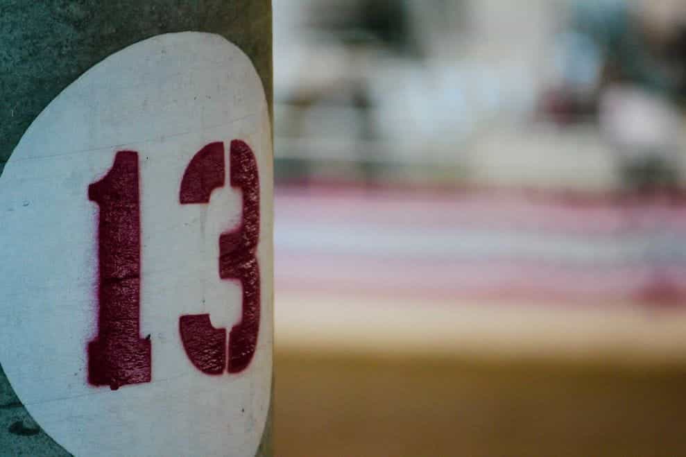 Nomor 13 disemprot dicat merah dengan stensil pada tiang abu-abu.