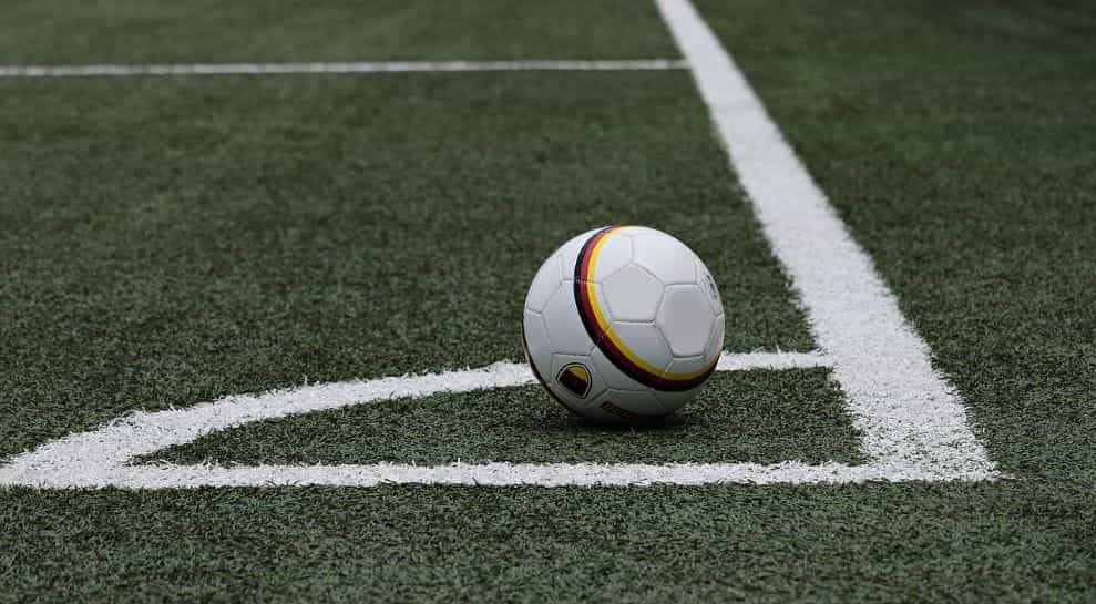 A soccer ball resting on a grassy pitch in the corner area of the pitch.