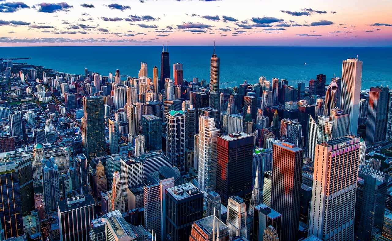 Area pusat kota Chicago yang padat, Illinois, dipenuhi gedung pencakar langit dan gedung-gedung tinggi, dengan Danau Michigan yang terbentang hingga cakrawala di latar belakang.