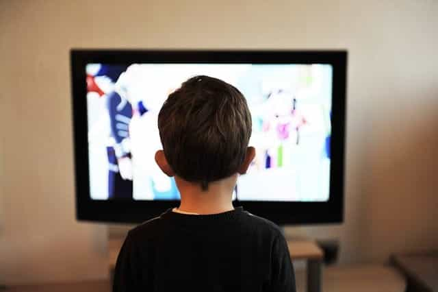 Bagian belakang seorang anak duduk di depan dan menonton layar televisi.