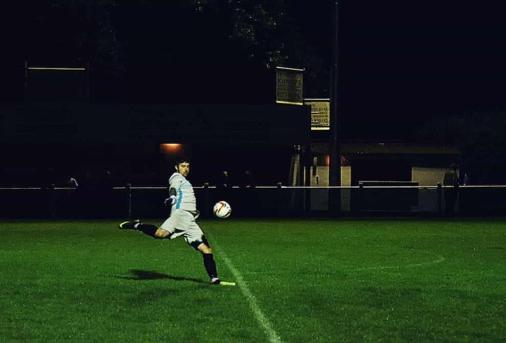 A footballer kicks a ball on a grass pitch.